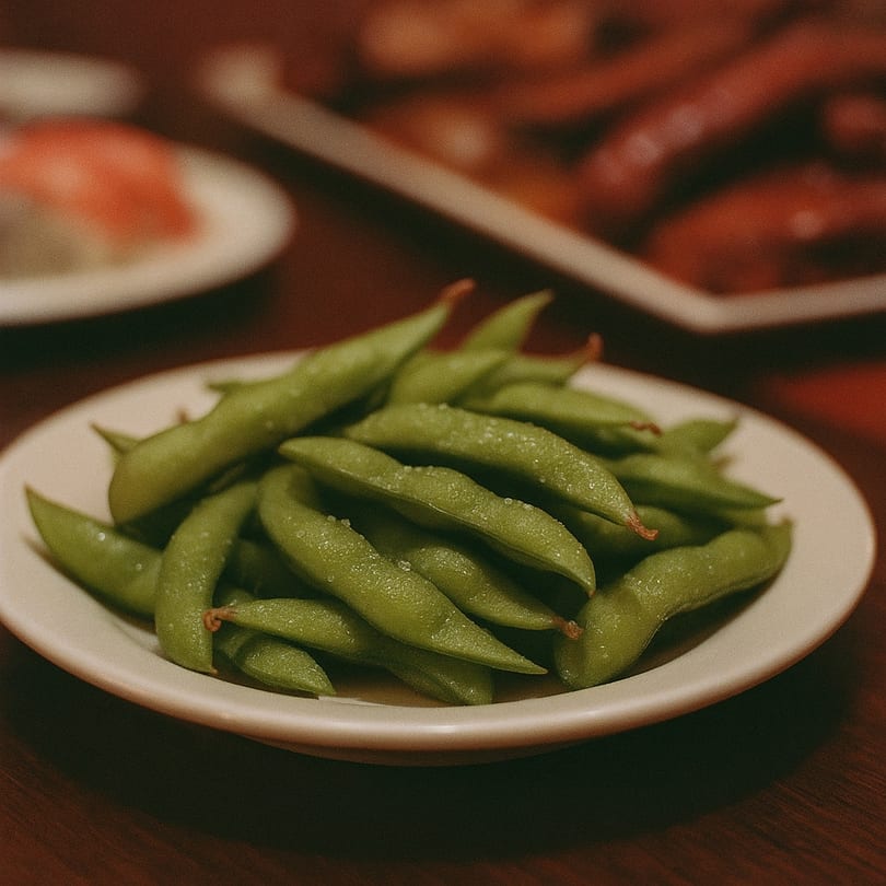 A white plate filled with salted edamame pods on a wooden table at Fuji Sushi & Grill.